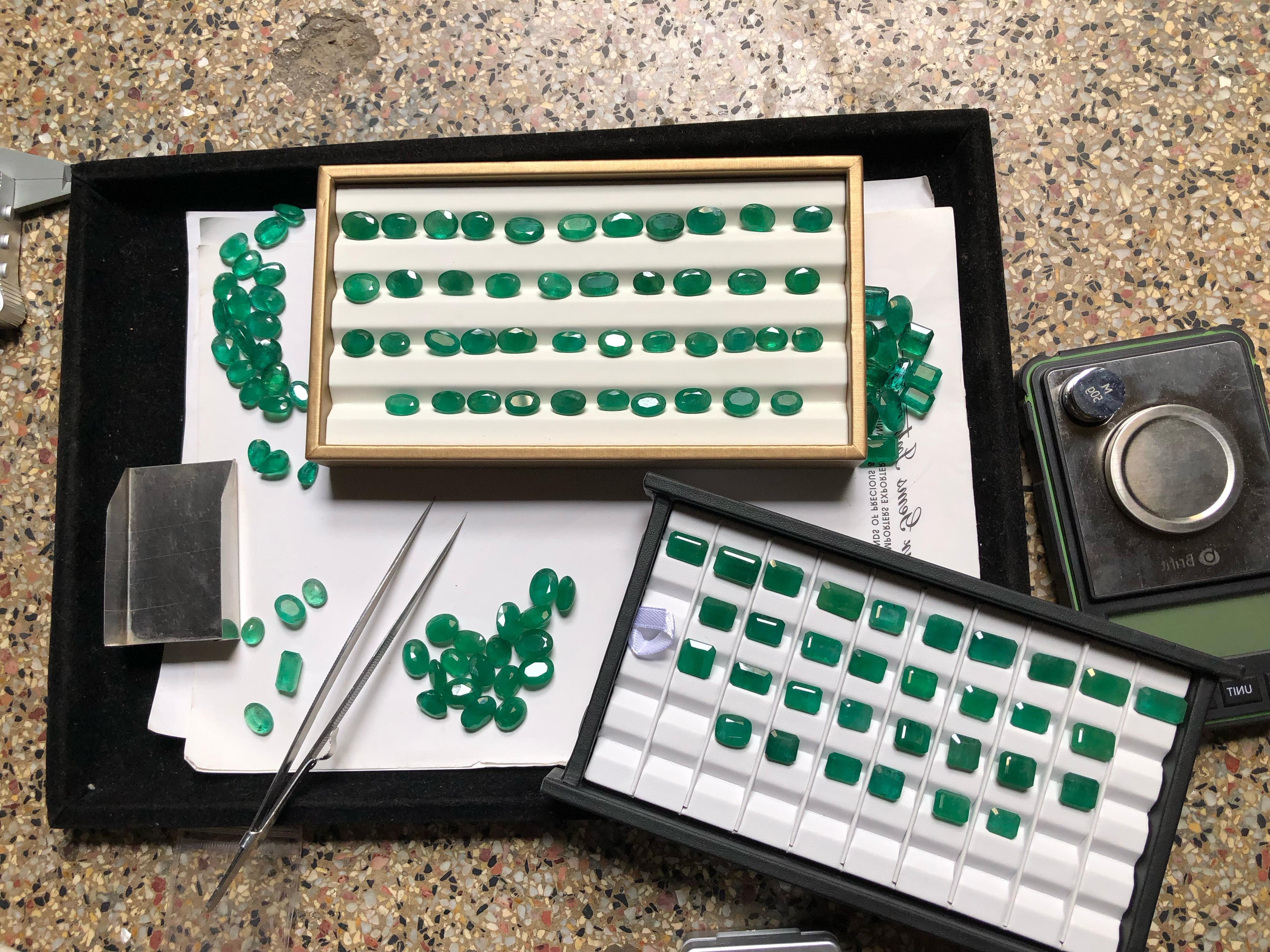 Collection of emerald gemstones in various displays on a speckled surface