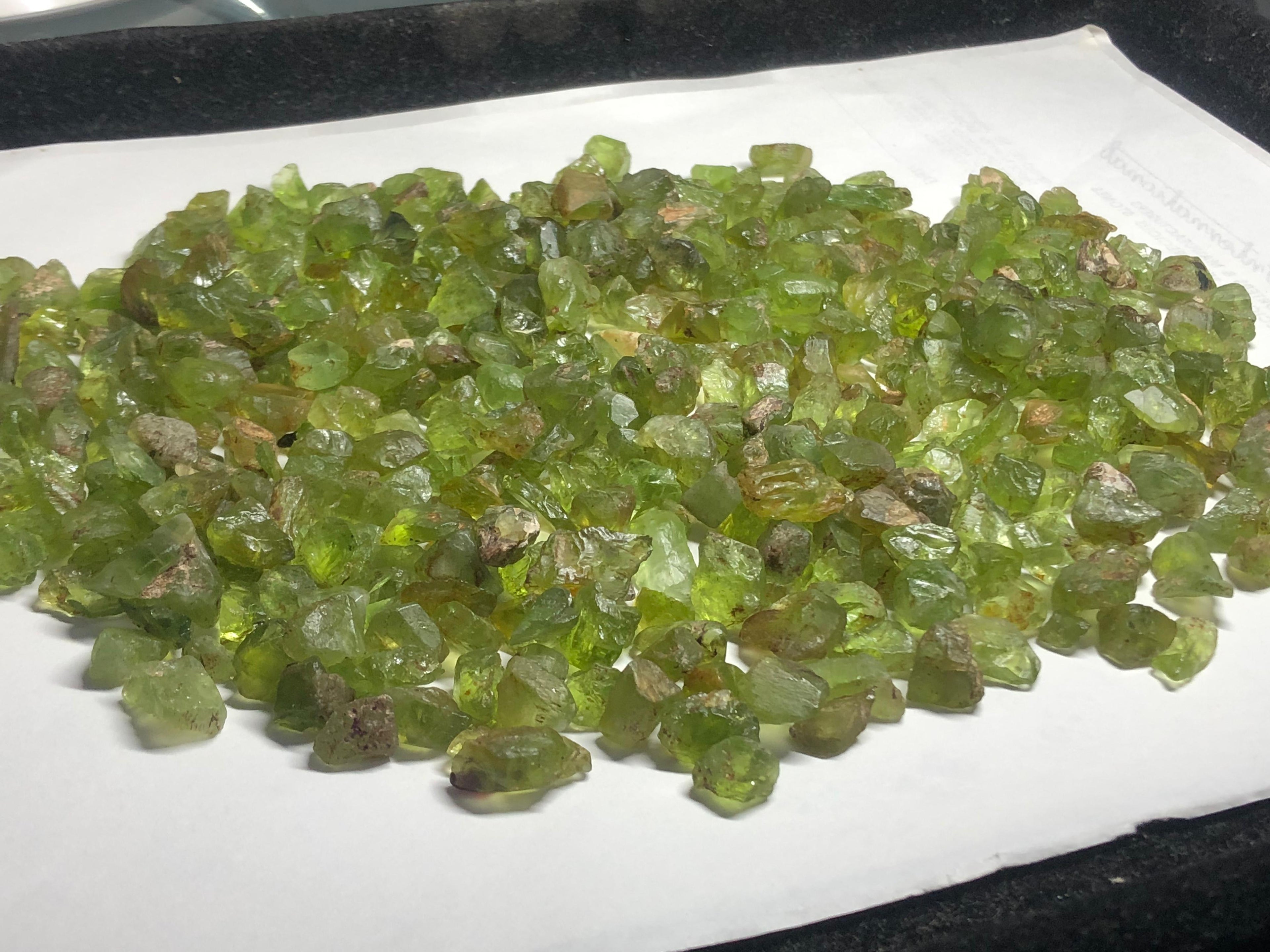 A heap of raw Peridots gemstones on a white surface
