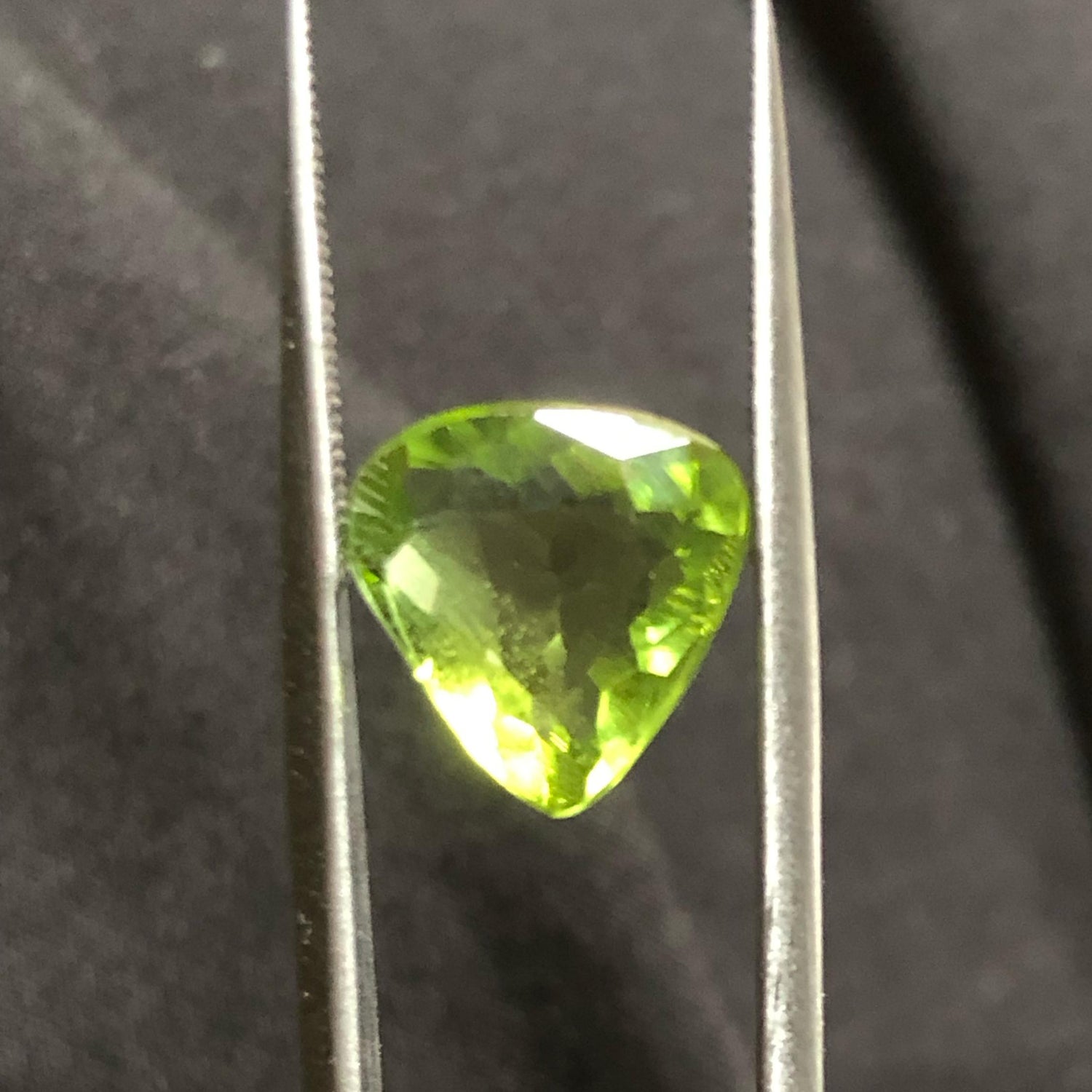 Peridot gemstone held between tweezers against a dark background