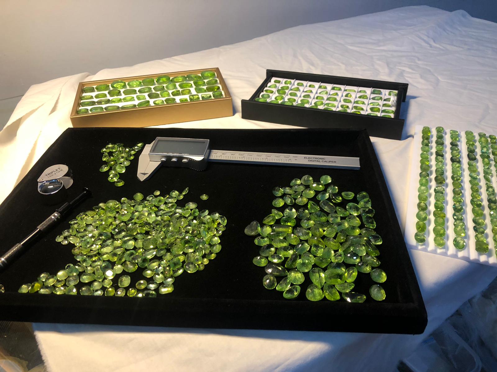 Peridot gemstones on trays with a measuring tool on a white cloth background