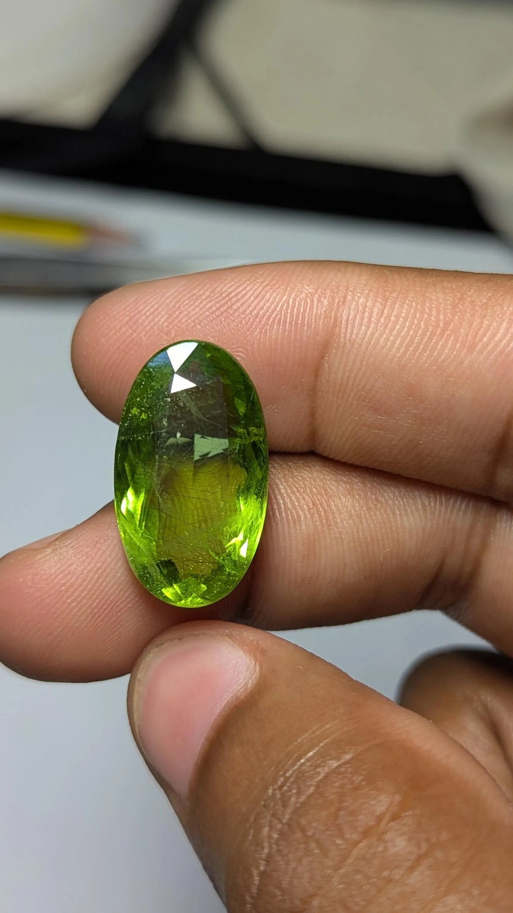 Peridot gemstone held between fingers against a neutral background