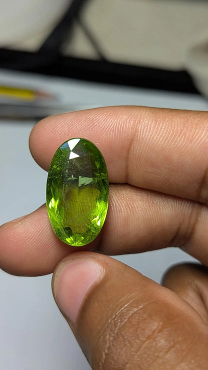 Peridot gemstone held between fingers against a neutral background
