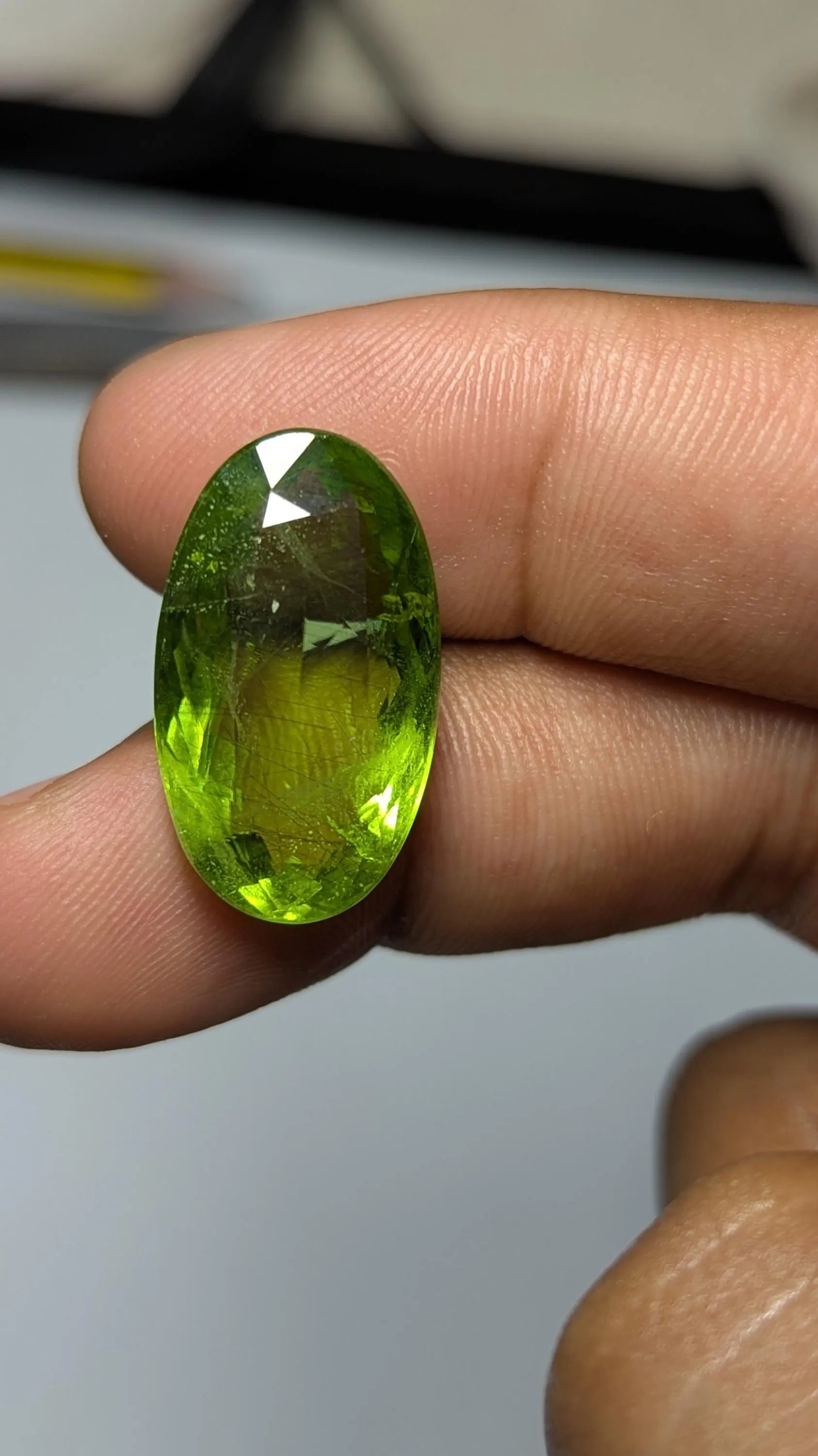 Peridot gemstone held between fingers against a neutral background