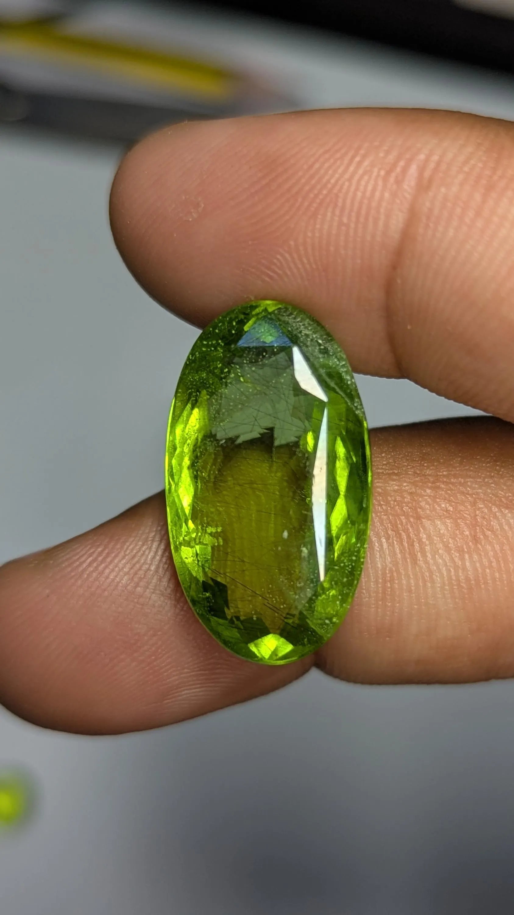 Peridot gemstone held between fingers against a neutral background