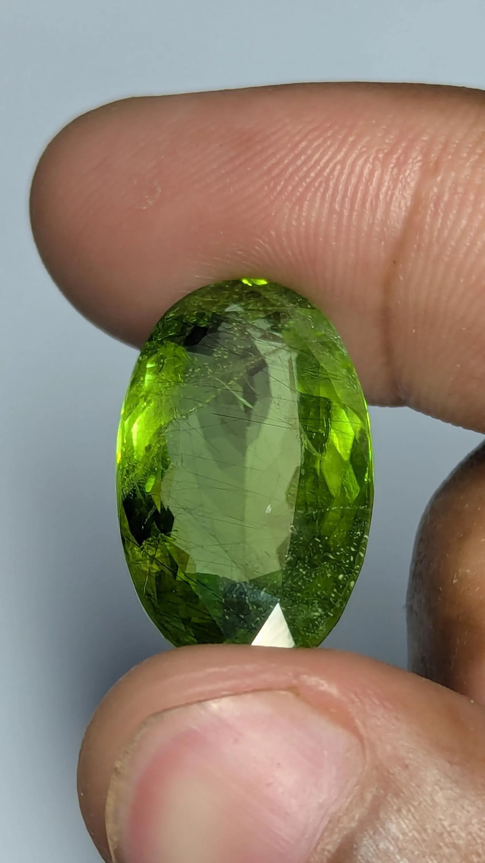 Peridot gemstone held between fingers against a neutral background