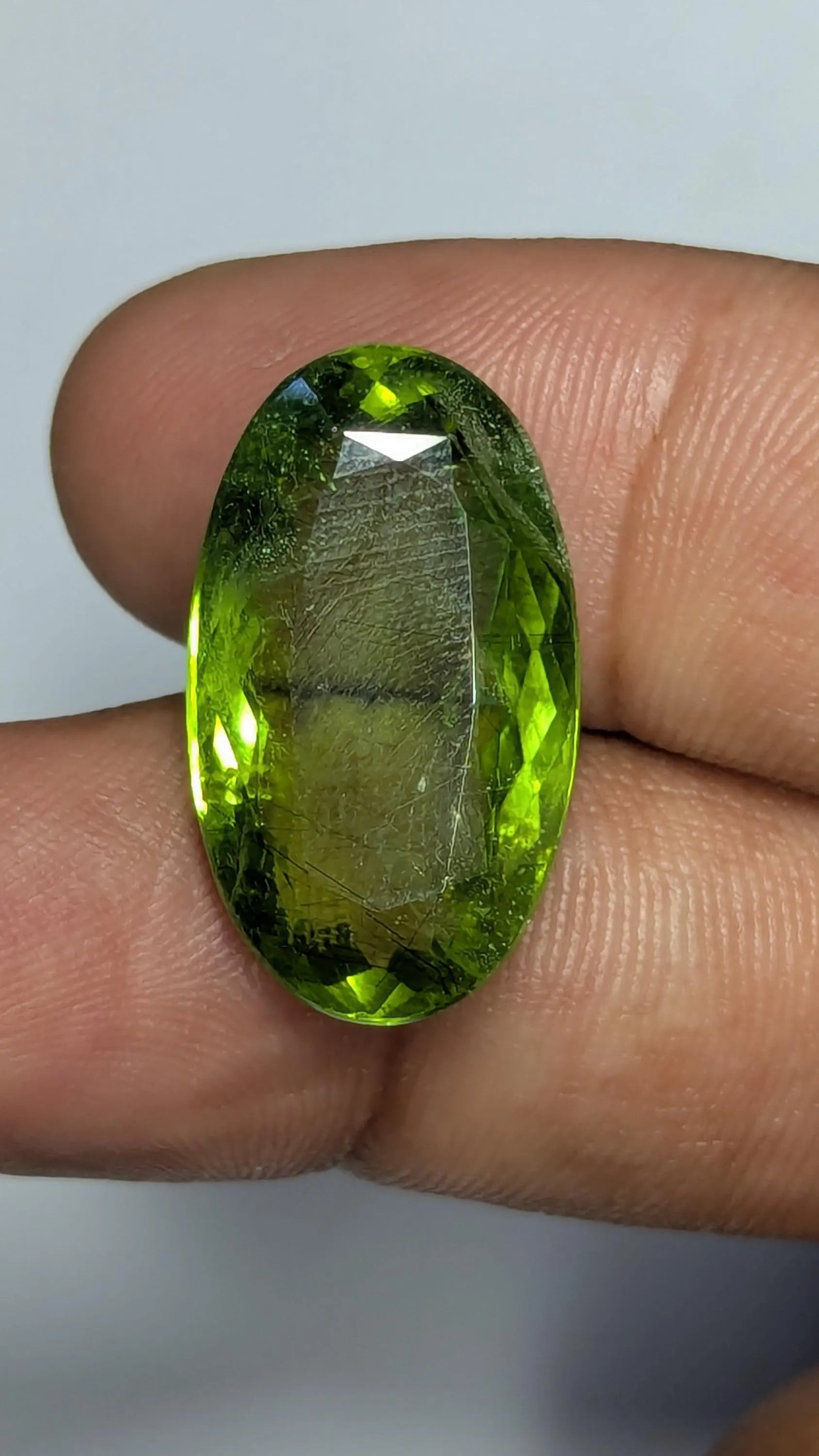Peridot gemstone held between fingers against a neutral background