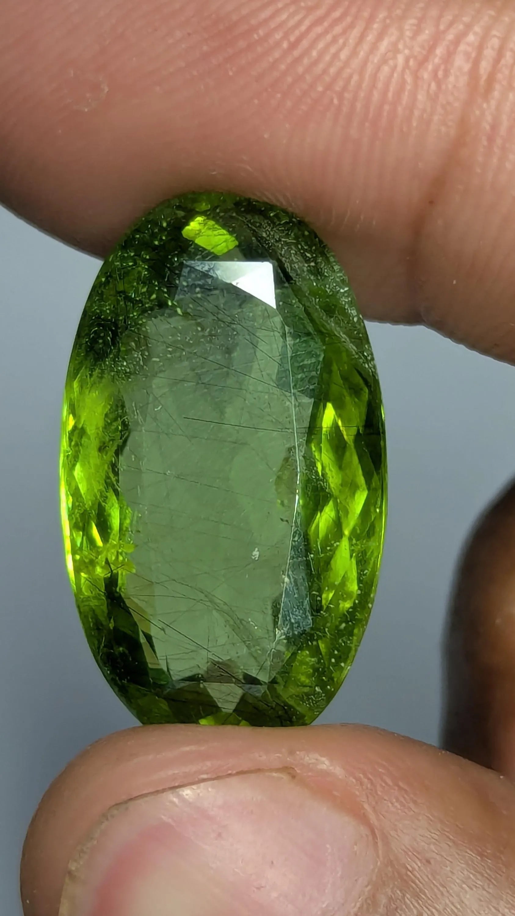 Peridot gemstone held between fingers against a neutral background