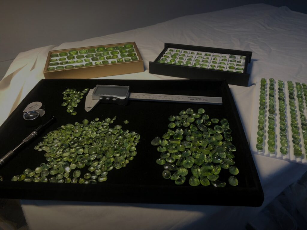 Natural Pakistani peridot gemstones — loose faceted peridots on a jeweler's tray at HM Gemscollection